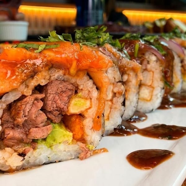 Sushi rolls with beef, avocado, and a sweet sauce on a white rectangular plate.