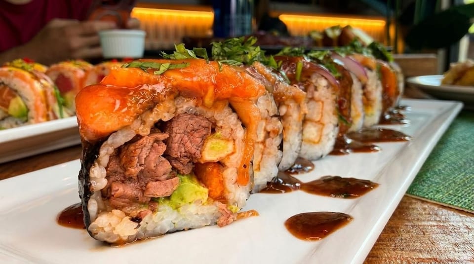 Sushi rolls with beef, avocado, and a sweet sauce on a white rectangular plate.