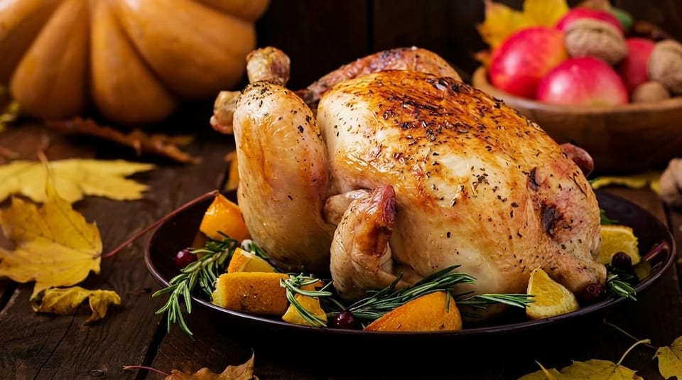 Roasted whole chicken garnished with oranges, rosemary, and cranberries on a rustic wooden table.